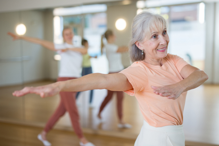 Senior woman performing contemporary dance during group training in studio.